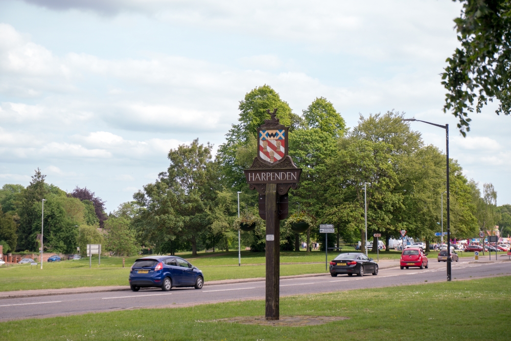Image of Harpenden village sign with road in background and trees